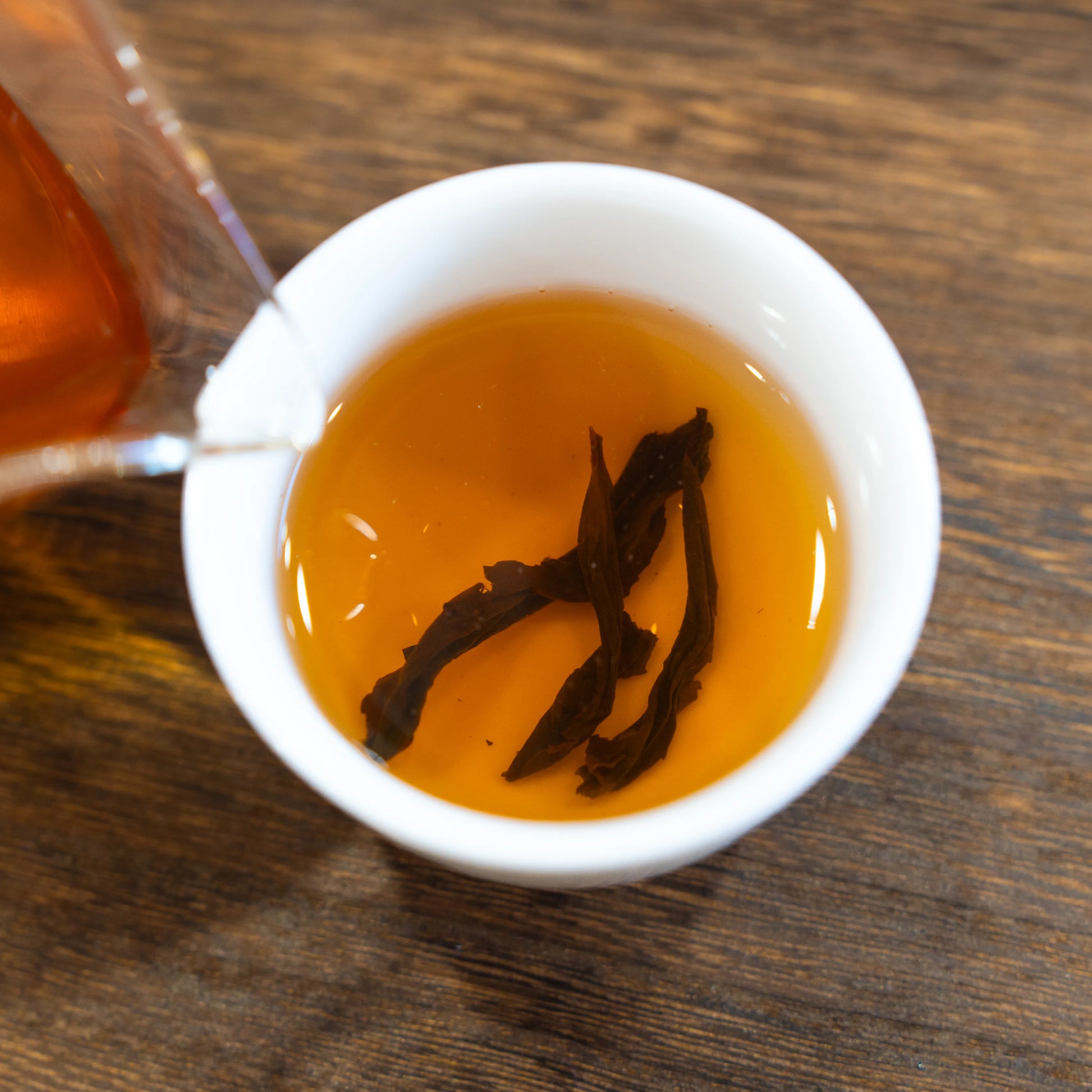 Brewed golden water turtle rock tea of rooteas being poured into a white cup on a wooden surface
