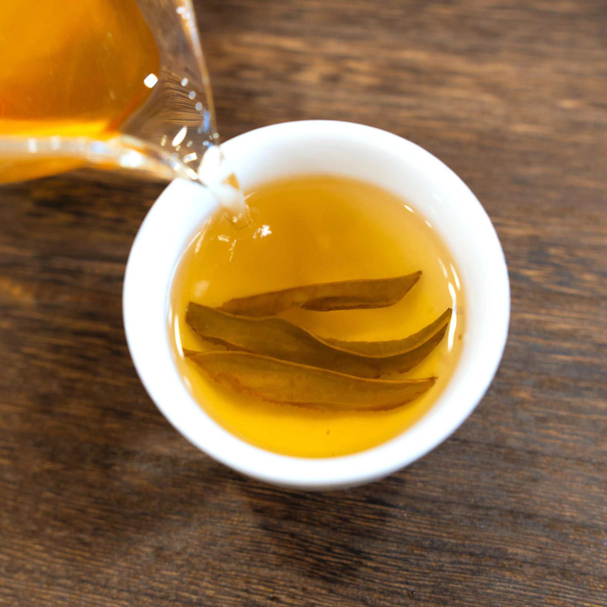 Brewed white cockscomb rock tea of rooteas being poured into a white cup on a wooden surface