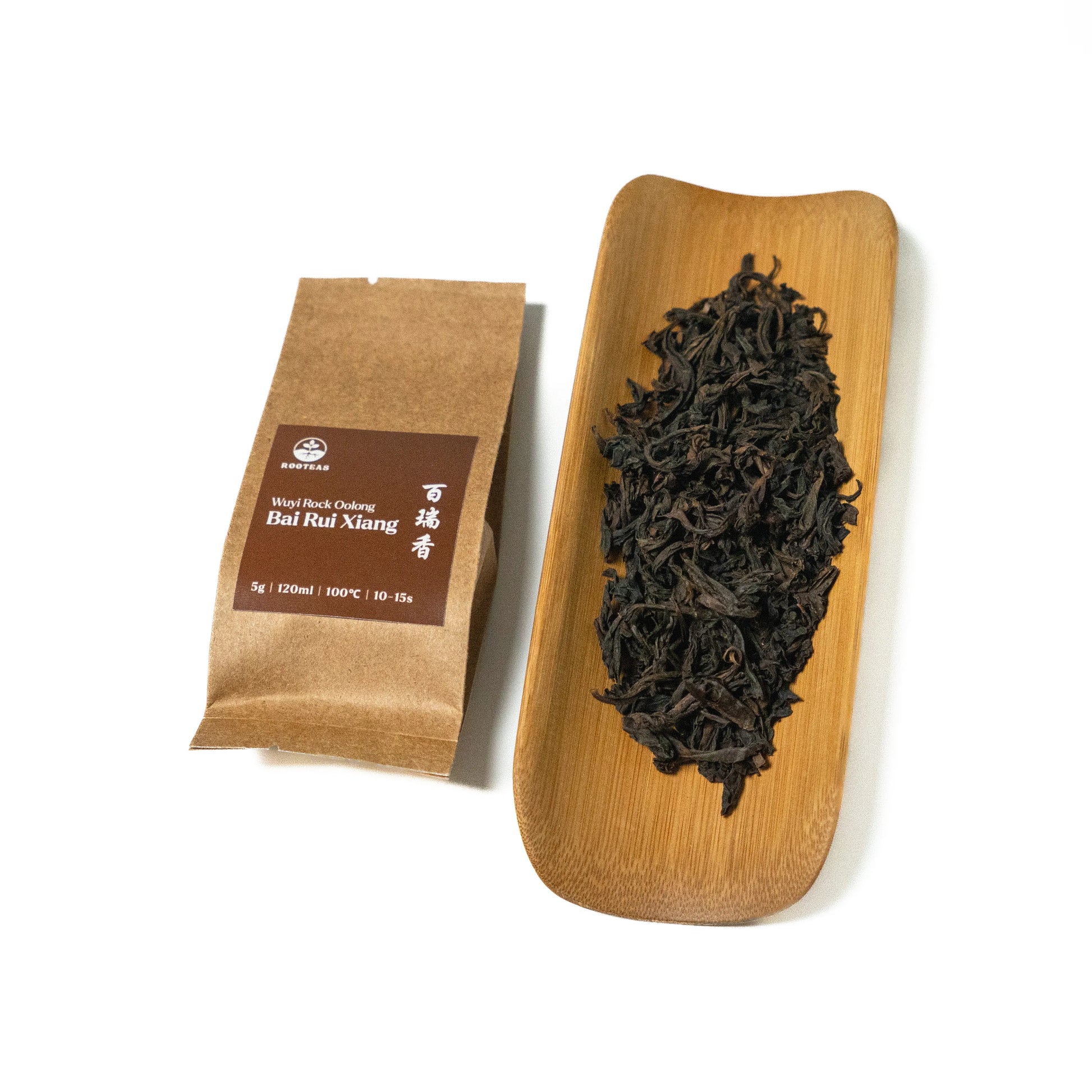 Dried rock oolong tea leaves on a wooden board with a brown packaging sleeve on a white background