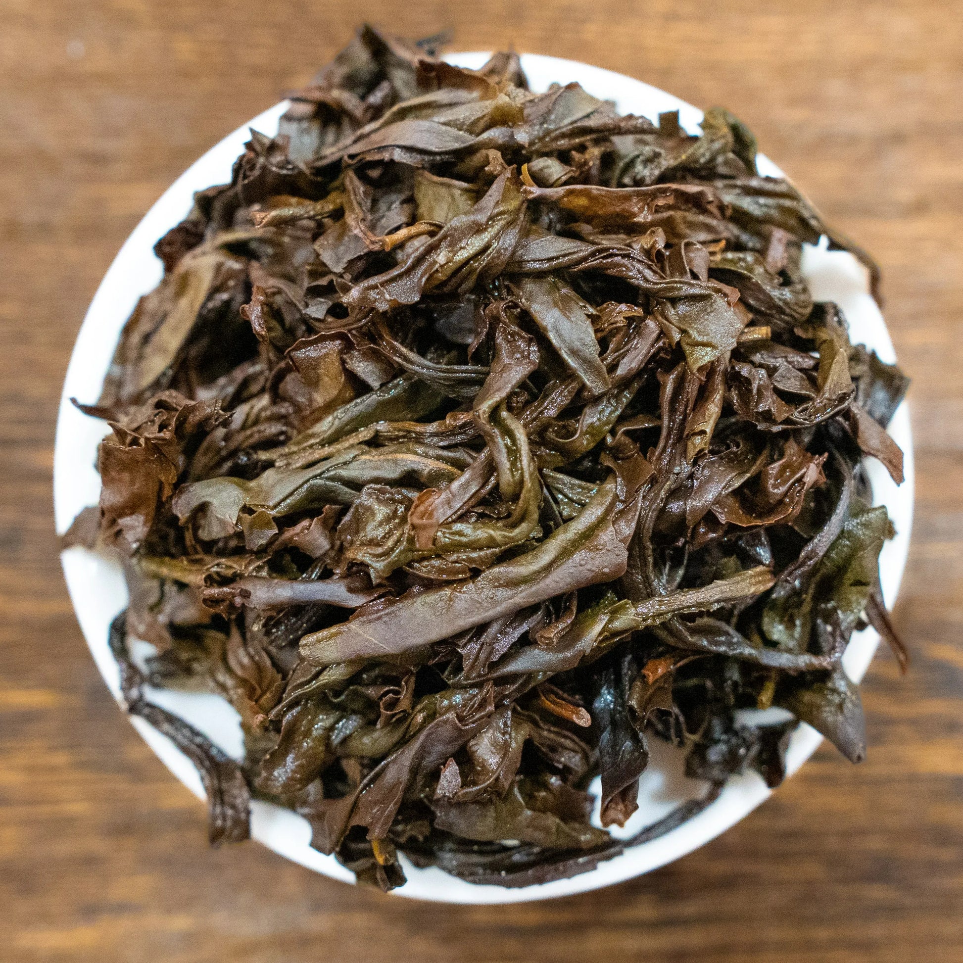 Rooteas brewed golden water turtle rock tea leaves on a white plate with a wooden background