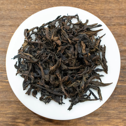 Rooteas dry golden water turtle rock tea leaves on a white plate with a wooden background
