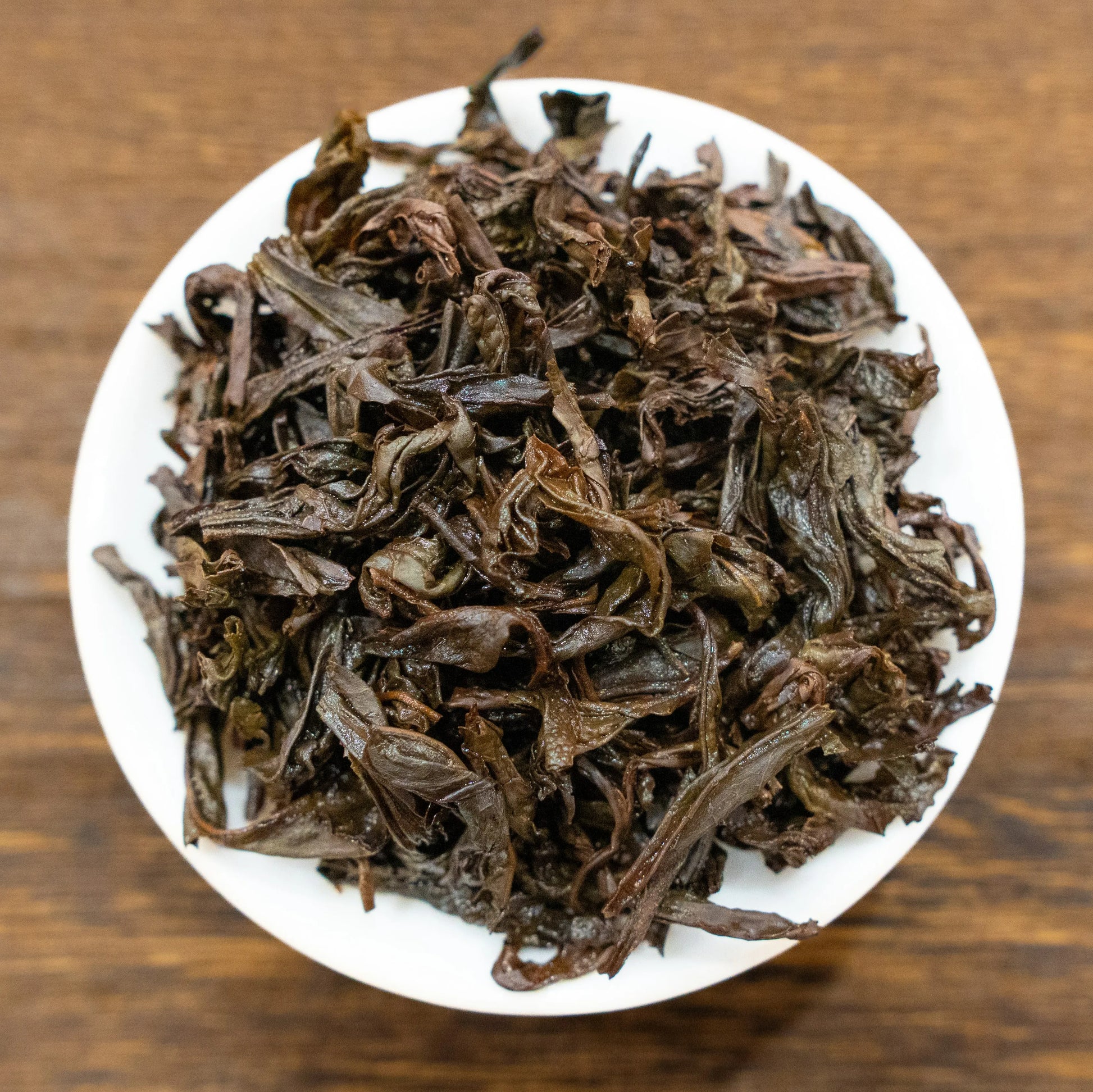 Rooteas brewed iron arhat rock tea leaves on a white plate with a wooden background