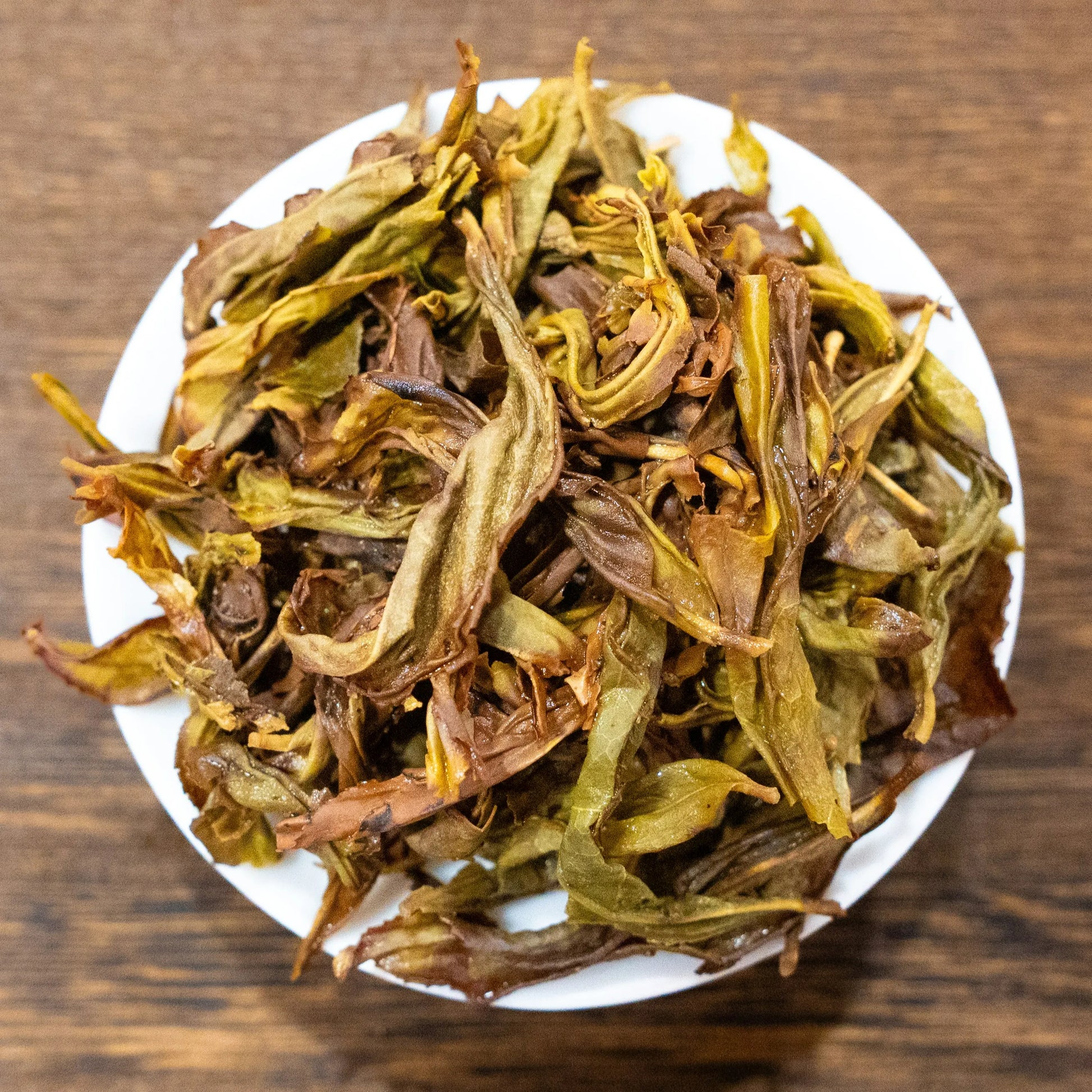 Rooteas brewed white cockscomb rock tea leaves on a white plate with a wooden background