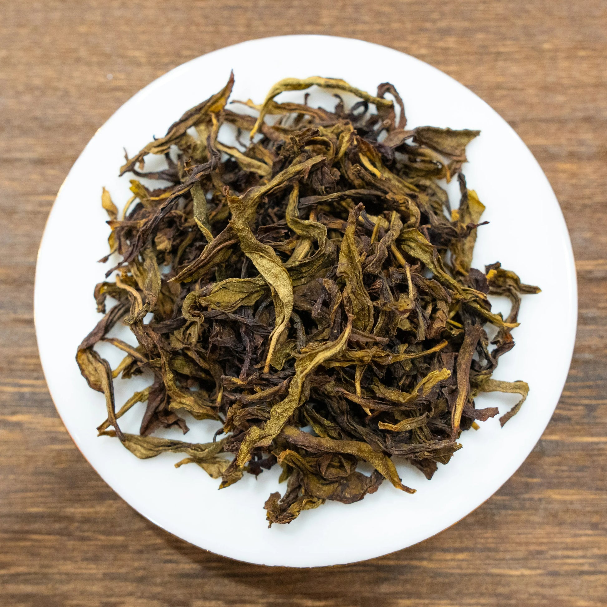 Rooteas dry white cockscomb rock tea leaves on a white plate with a wooden background