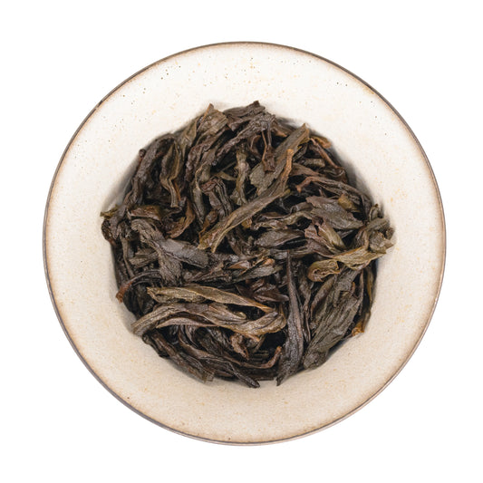 Wet wu san di lao cong shui xian tea leaves in a white gaiwan on a white background